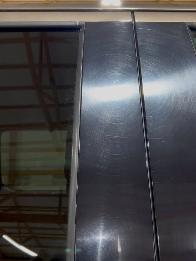 Black window pillar trim covered in fine swirl marks and haze before paint correction