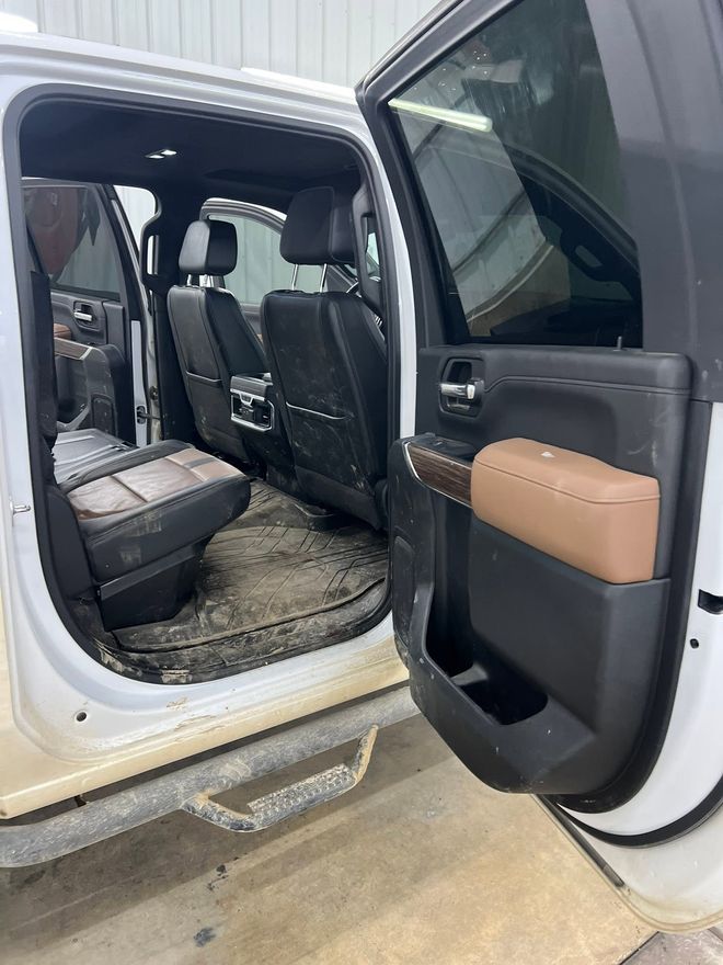 Rear cab of a white crew-cab truck with mud caked across the floor mat, door sill and seat backs
