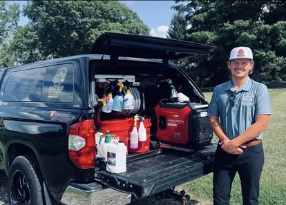 Carter Record beside his branded truck with the bed open, showing the generator, water containers and detailing products he brings to every job